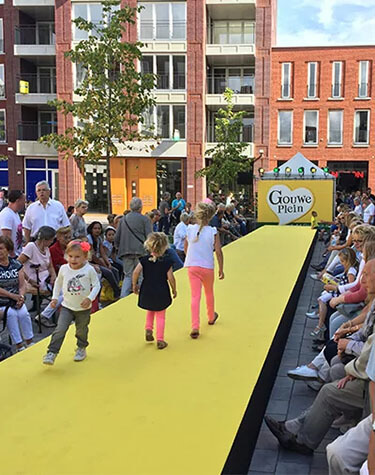 Drie jonge kinderen lopen over een gele catwalk omringd door toeschouwers