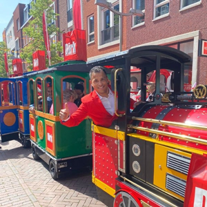 en kleurrijke kindertrein met enthousiaste bestuurder in rood kostuum, ingezet voor promotie bij Dirk supermarkten.